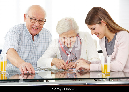 Eine junge Sozialarbeiterin Lösung Puzzle mit älteres paar zu Hause Stockfoto