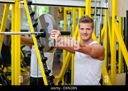 Hübschen jungen Mann im Fitnessstudio, Hantel, Gewicht Disck aufsetzen Blick in die Kamera Lächeln Stockfoto