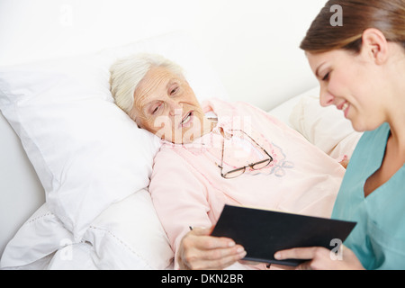 Geriatrische Krankenschwester Lesebuch Seniorin Frau im Bett Stockfoto