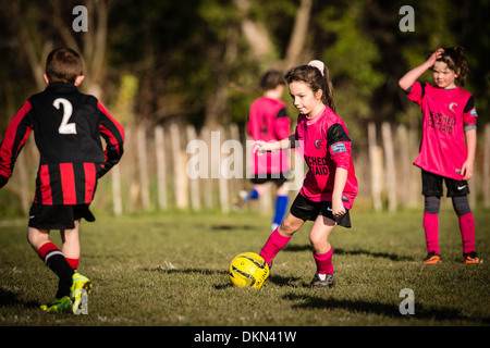Grundschule im Alter von jungen und Mädchen spielen wettbewerbsfähige Fußball im Park an einem Samstagmorgen, UK Stockfoto