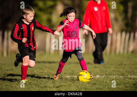 Grundschule im Alter von jungen und Mädchen spielen wettbewerbsfähige Fußball im Park an einem Samstagmorgen, UK Stockfoto