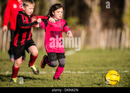 Grundschule im Alter von jungen und Mädchen spielen wettbewerbsfähige Fußball im Park an einem Samstagmorgen, UK Stockfoto