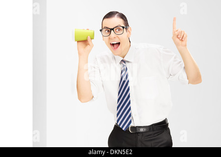 Lächelnder Mann mit Brille, durch die Wand mit einer Tasse hören Stockfoto