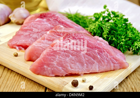 Drei Stück von Schweinefleisch, Knoblauch, Petersilie, Dill, Messer, Pfeffer auf Holzbrettern Hintergrund Stockfoto