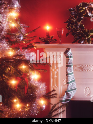 Weihnachten eines Kindes Strumpf auflegen auf einem kaminsims Neben einem geschmückten Weihnachtsbaum mit Kerzenlicht und ein Glas Sherry für Santa Claus. Stockfoto