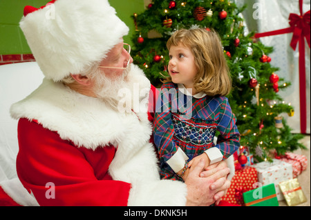 Santa Claus mit einem jungen Mädchen 6 7 8 9 auf seinem Schoß auf einem Stuhl zu ihm reden, was sie zu Weihnachten wünscht Stockfoto
