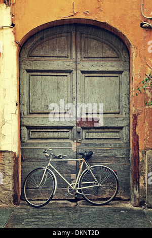 Vertikal ausgerichtete Bild Fahrrad gelehnt alte Holztür am Eingang zum Haus an regnerischen Tag in Alba, Italien. Stockfoto