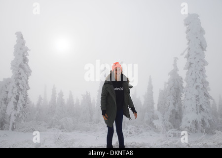 Weibliche Touristen balancieren auf einem Snowbank von Schnee bedeckt Bäume auf dem Dalton Highway Alaska mit Sonne durch den Nebel Stockfoto