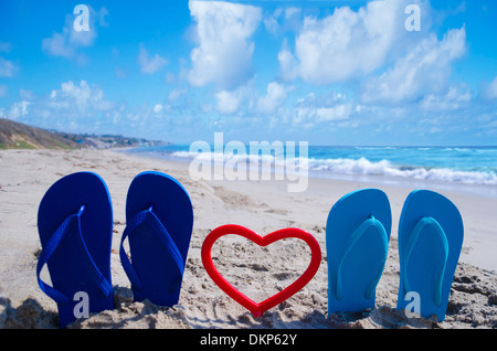 Flip-Flops mit Herzform am Sandstrand am Meer Stockfoto