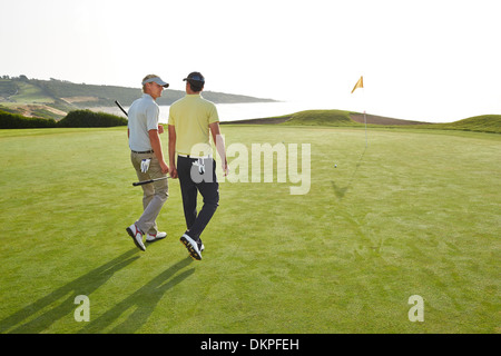 Männer, die zu Fuß in Richtung Loch am Golfplatz mit Blick auf Meer Stockfoto