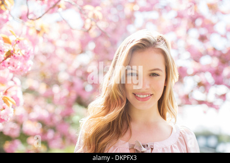 Frau lächelnd unter Baum mit rosa Blüten Stockfoto