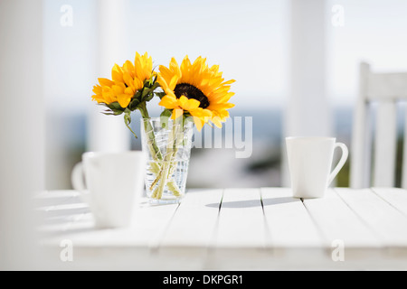 Vase mit Blumen und Kaffeetassen auf Küchentisch Stockfoto