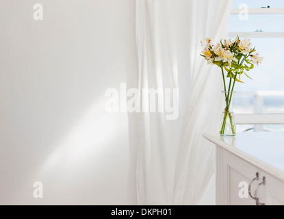 Vase mit Blumen auf Schreibtisch im weißen Raum Stockfoto