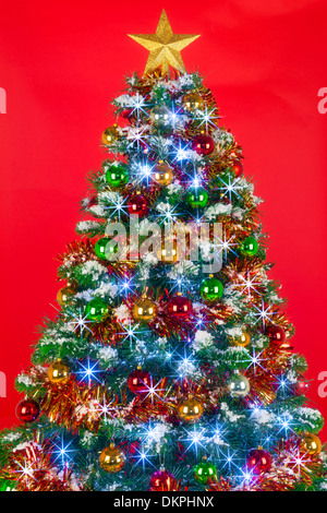 Ein geschmückter Weihnachtsbaum mit Kugeln, Lametta und Lichterketten auf rotem Grund. Stockfoto