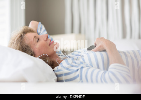 Ältere Frau hören Kopfhörer auf Bett Stockfoto