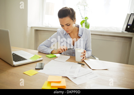Attraktive junge Frau an der Rezeption mit Haftnotizen und Laptop. Schöne Geschäftsfrau Notenlesen beim Sitzen Stockfoto