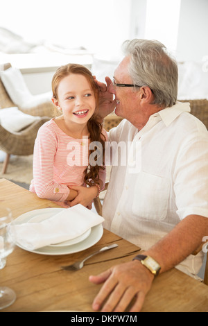 Älterer Mann und Enkelin Flüstern am Tisch Stockfoto