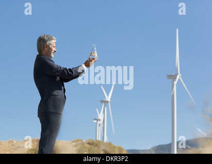 Geschäftsmann mit Glas Wasser durch Windkraftanlagen in ländlichen Landschaft Stockfoto