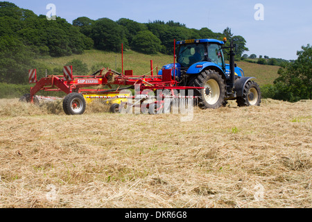 Auftragnehmer mit einem Traktor von New Holland T7030 und einen SIP-Heu-Rechen, Rechen Heu Pressen auf einem Bio-Bauernhof. Powys, Wales. Juli. Stockfoto