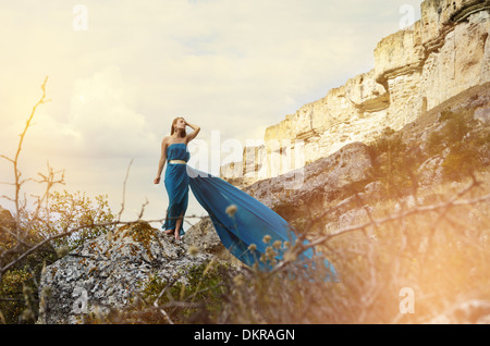 Junge schöne allein Frau im dunklen blaugrünen Kleid steht auf dem Felsen mit Bergen im Hintergrund Stockfoto