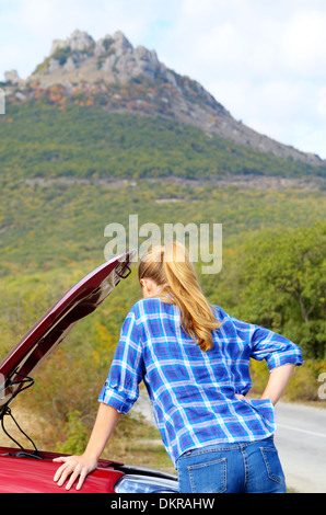 Junge Frau in der Nähe von kaputten Auto braucht Hilfe suchen unter geöffneter Haube Stockfoto