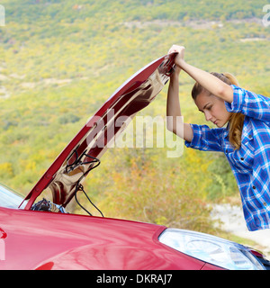 Junge Frau in der Nähe von kaputten Auto braucht Hilfe suchen unter geöffneter Haube Stockfoto