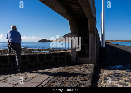 Alter Mann ruht auf Wand, Blick auf das Meer, eingerahmt in eine Wandanlage in el Medano, Teneriffa, Kanarische Inseln, Spanien Stockfoto