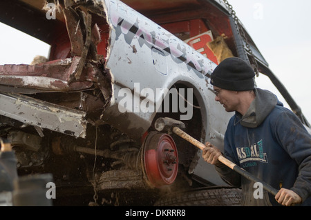 Mann mit einem Vorschlaghammer, Körperarbeit, Weg von den Rädern auf einem Stockcar Auto zu schlagen Stockfoto