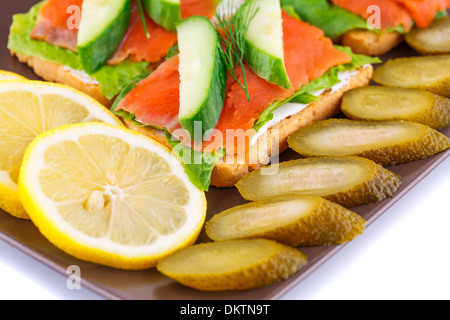 Lachs Sandwiches mit Salat, frische und eingelegte Gurken, Zwiebel, Zitrone auf Platte. Stockfoto