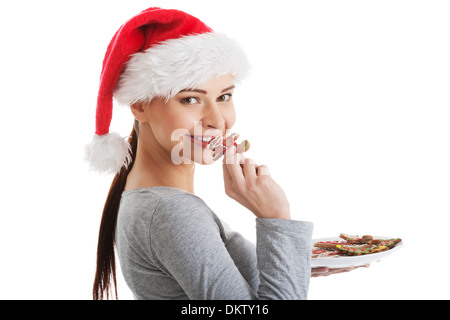 Schöne Frau in Essen einen Cookie Weihnachtsmütze. Isoliert auf weiss. Stockfoto