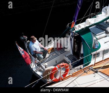 Mann mit Kappe sitzt auf seiner Yacht in der Sonne, als Er reist die neptunes Treppe Caledonian cansl schottischen Highlands Stockfoto