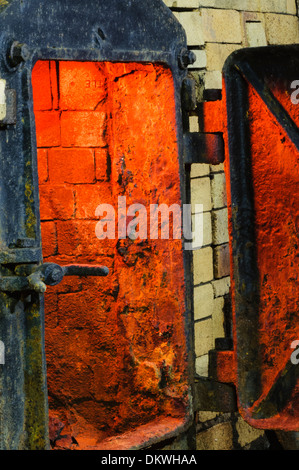 Gusseisernen Tür einen großen Ofen Brennofen Müllverbrennungsanlage aus Ziegeln, mit dem Schein des Feuers innen hergestellt. Stockfoto