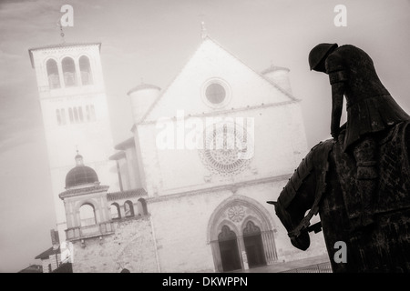 Morgennebel schafft eine stimmungsvolle Kulisse für diese Statue eines Ritters auf dem Pferderücken vor der Basilika San Francesco von Assisi. Stockfoto