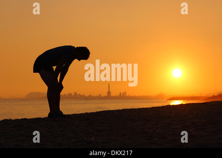 Silhouette der ein müde Sportler bei Sonnenuntergang mit einer Stadt im Hintergrund Stockfoto