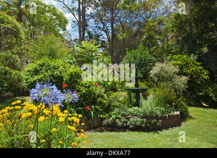 Spektakuläre subtropischen Bauerngarten - dekorative Brunnen Wasserspiel, smaragdgrüne Blätter, blühende Sträucher, Stauden, Rasen Stockfoto