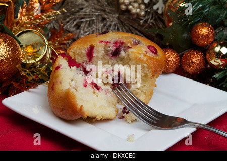 Frische hausgemachte Cranberry Muffins auf einem weißen Teller setzen auf eine saisonale Weihnachtstisch mit Dekorationen und einer roten Tischdecke. Stockfoto