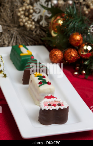 Eine Auswahl individueller Weihnachtskuchen auf einem weißen Teller mit saisonalen Dekorationen auf einer roten Tischdecke Stockfoto