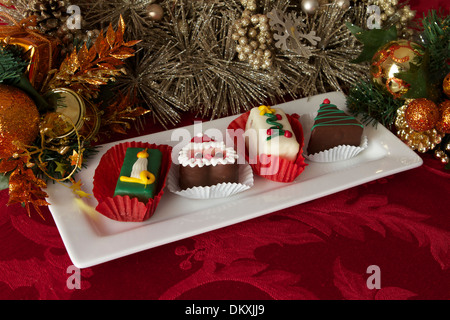 Eine Auswahl individueller Weihnachtskuchen auf einem weißen Teller mit saisonalen Dekorationen auf einer roten Tischdecke Stockfoto