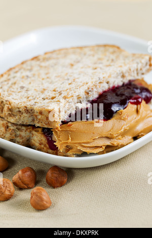 Closeup vertikale Foto eines Erdnussbutter und Marmelade Sandwich halbieren, in weißen Teller mit ganzen Nüssen Stockfoto