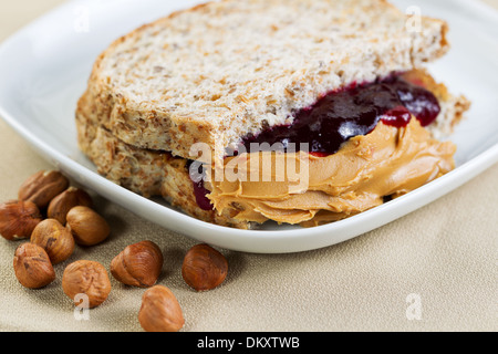 Closeup horizontale Foto eines Erdnussbutter und Marmelade Sandwich halbieren, in weißen Teller mit ganzen Nüssen Stockfoto