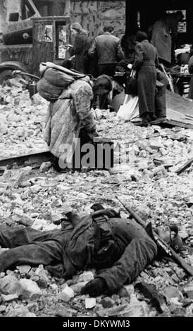 Frauen und Männer der Berliner Bevölkerung suchen nach Dingen, die im April/Mai 1945 noch in den Ruinen der Stadt verwendet werden können. Im Vordergrund steht ein toter Soldat der deutschen Wehrmacht. Fotoarchiv für Zeitgeschichte Stockfoto