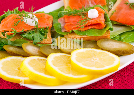 Lachs Sandwiches mit Salat, frische und eingelegte Gurken, Zwiebel, Zitrone auf Platte. Stockfoto