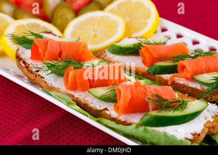 Lachs Sandwiches mit Salat, frische und eingelegte Gurken, Zwiebel, Zitrone auf Platte. Stockfoto