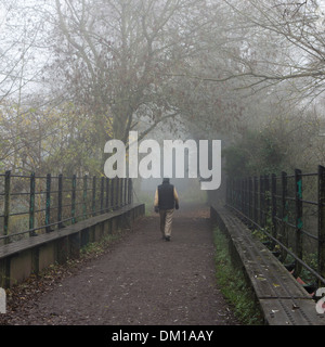Winterwanderung: ein einsamer Mann geht auf eine Brücke in Nebel, an einem Wintertag. Stockfoto
