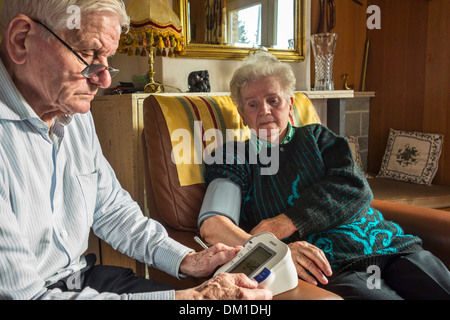 Nahaufnahme eines älteren Ehepaares, die Überprüfung ihrer eigenen Blutdrucks mit einem digitalen Blutdruckmessgerät im Wohnzimmer zu Hause Stockfoto