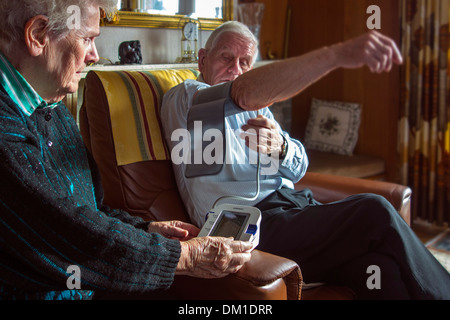 Nahaufnahme eines älteren Ehepaares, die Überprüfung ihrer eigenen Blutdrucks mit einem digitalen Blutdruckmessgerät im Wohnzimmer zu Hause Stockfoto