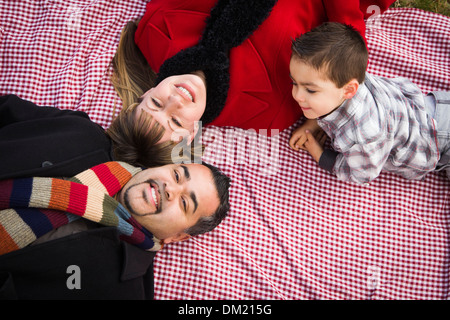 Young gemischt Rennen Familie in Winterkleidung Verlegung auf dem Rücken auf der Picknickdecke im Park zusammen. Stockfoto