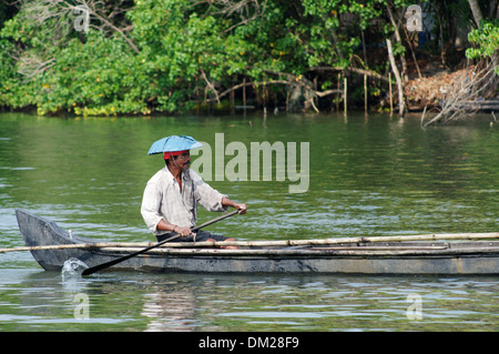 Ein indischer Mann mit einem Sonnenschirm-Hut mit dem Kanu in den Backwaters von Kerala in Indien Stockfoto