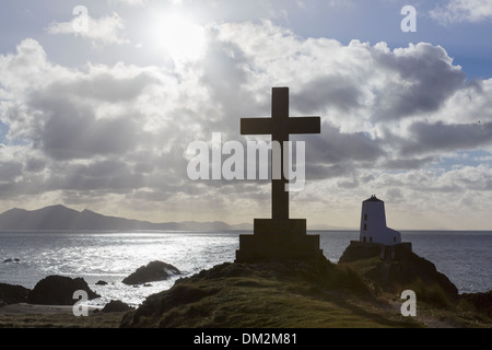 Steinkreuz und der alte Leuchtturm (Twr Mawr) in Silhouette gegen Sonnenschein auf Ynys Llanddwyn Island, Rhosneigr, Isle of Anglesey, North Wales, UK Stockfoto