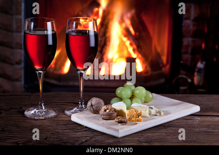 Romantisches Stilleben am Kamin. Gläser Wein, Käse und Nüssen. Stockfoto